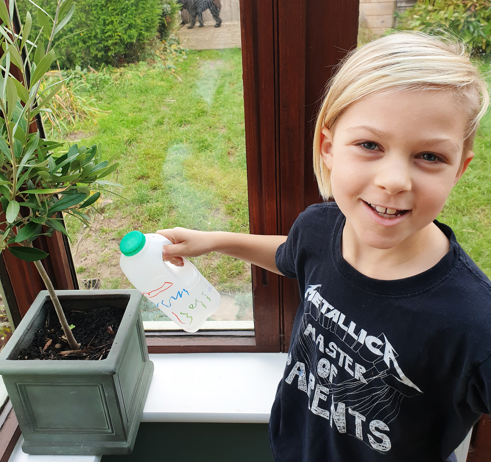 A child watering a plant with their decorated milk bottle watering can 