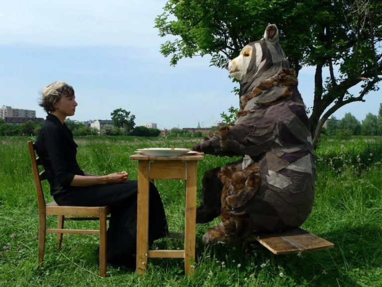 gaganis - Women sitting at table opposite person in bear costume