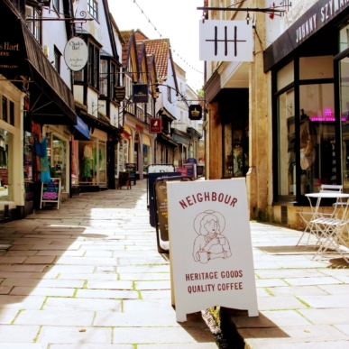 a view looking up Cheap Street in Frome, with Shop advertising boards straddling the leat.